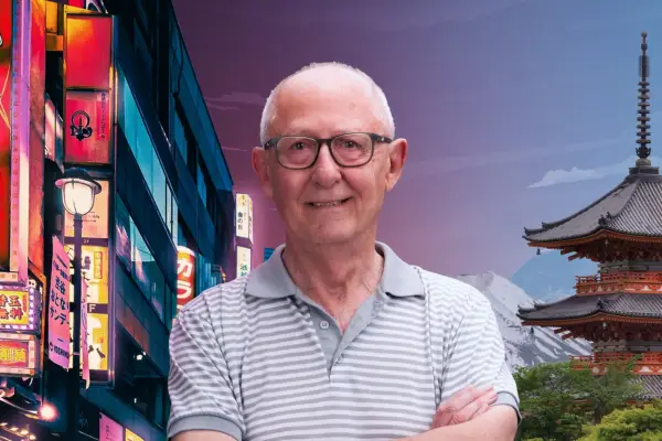 Pensioner with grey hair and glasses smiles at camera with scene of Japan behind him.