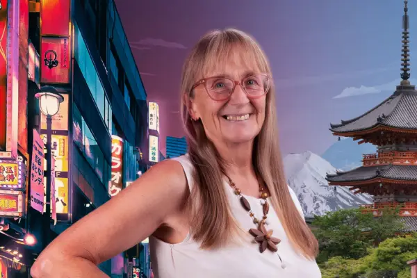 Pensioner with light brown hair smiles at camera with scene of Japan behind her.