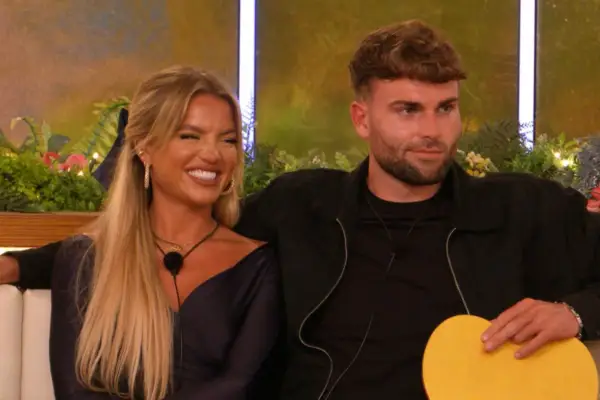 Molly Smith and Tom Clare looking across and smiling at something. They are both wearing all black and have microphones around their necks.