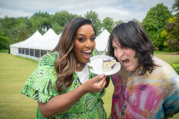 Noel Fielding and Alison Hammond standing together, pretending to eat a slice of cake