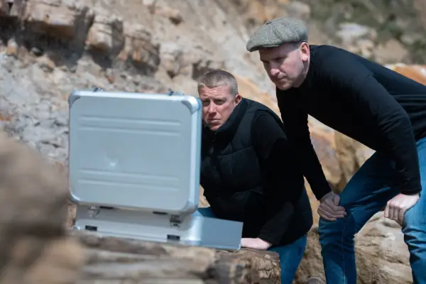 Joey and James on 007: Road To A Million looking into a silver case