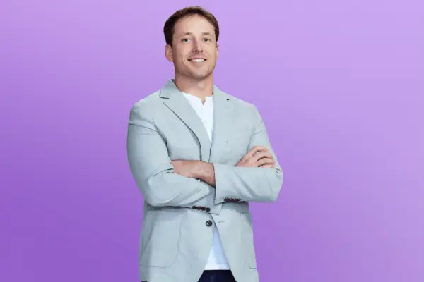 Jeramey in a light blue blazer with his arms crossed in front of a purple background