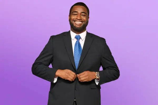 Dayo wearing a black suit and blue tie, smiling ahead.