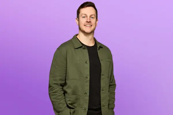 Logan wearing a black t-shirt and a green overshirt, smiling ahead with his hands in his pockets.