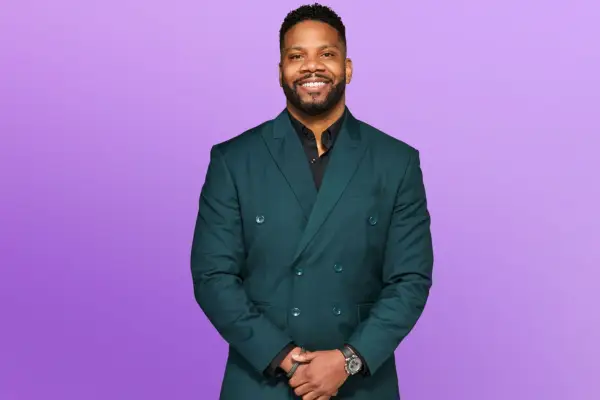 Michael wearing a dark blue double breasted suit, smiling ahead with his hands placed in front of him.