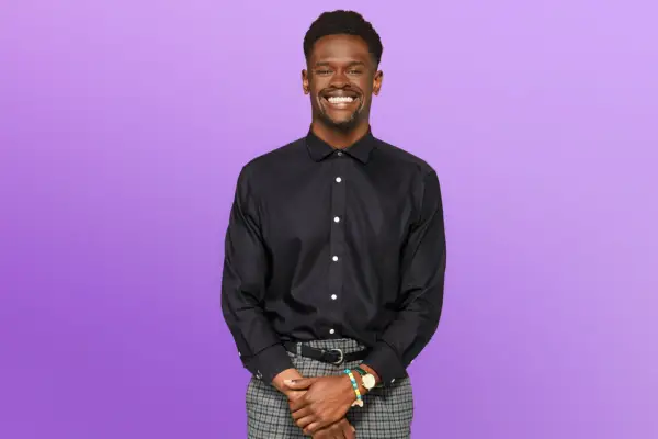 Edmond wearing a black shirt and grey trousers, smiling ahead.