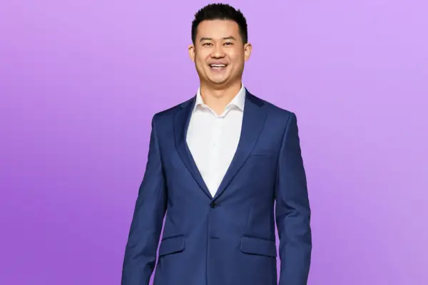 Patrick wearing a white shirt and blue blazer, smiling ahead.