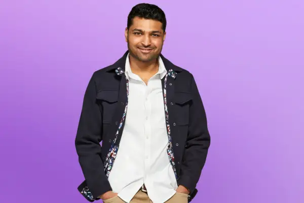 Rohan wearing a white shirt and black jacket, smiling ahead with his hands in his pockets.
