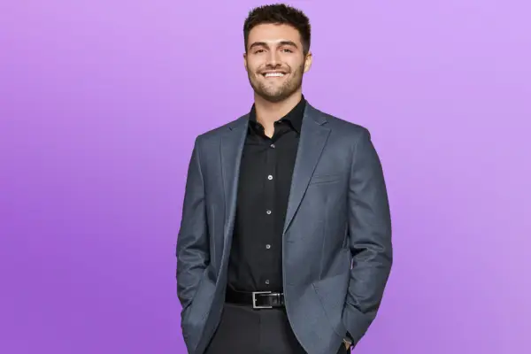 Joe wearing a dark suit, smiling ahead with his hands in his pockets.