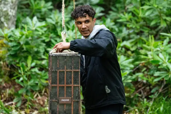 Freddie on The Traitors holding a block that is being suspended in the air by a rope.