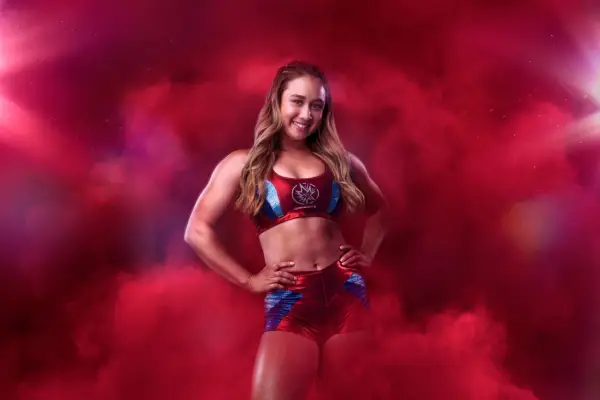 Dynamite AKA Emily Steel stood posing with her hands on her hips as she is surrounded by red smoke.
