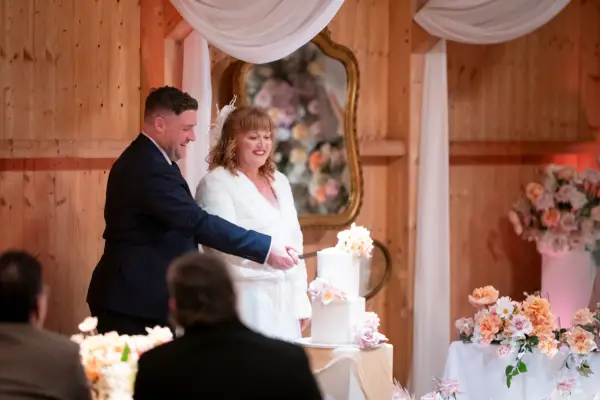 A bride and groom stood next to each other holding a knife, cutting a wedding cake.