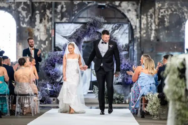Jamie and Dave ind wedding attire, holding hands as they walk down the aisle.