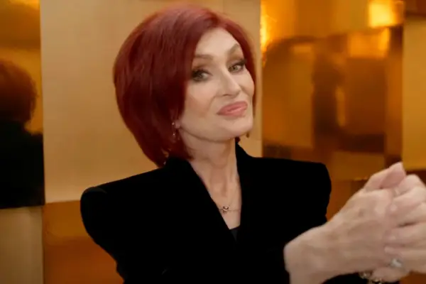 Sharon Osbourne making a mixing motion with her hands. She is wearing a black outfit and is smiling ahead
