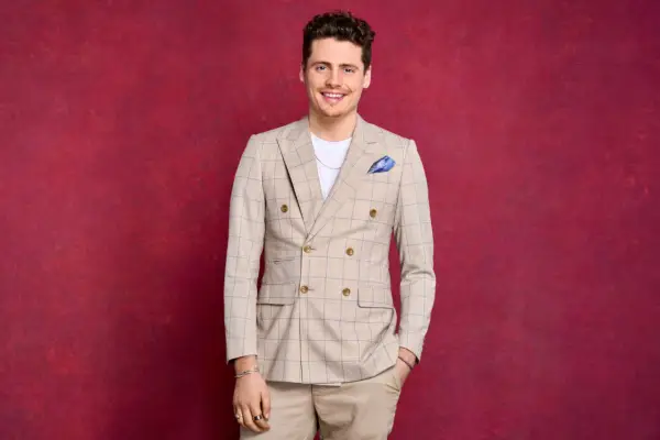 Angus Findlay wearing a brown suit, smiling ahead with his hand in his pocket.