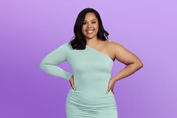 Alejandra is in a long blue dress posing in front of a purple background