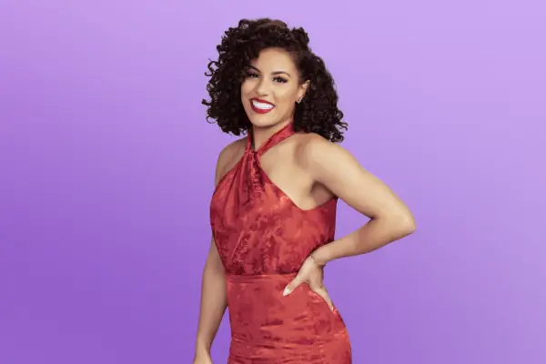Danette in a long red dress posing with her hand on her hip in front of a purple background