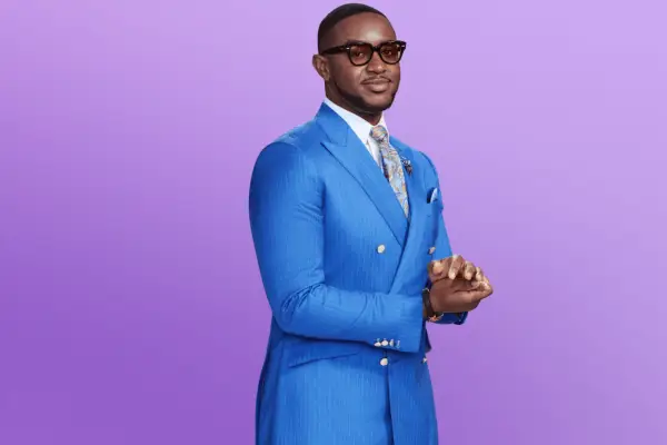 Jamal in an all-blue suit holding his hands together posing in front of a purple background