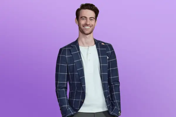 Nolan in a checkered blazer and white t-shirt in front of a purple background