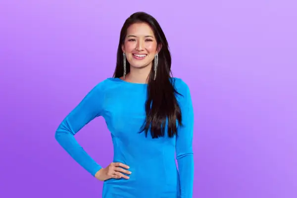 Clay in an all-orange suit with his hands together, posing in front of a purple background