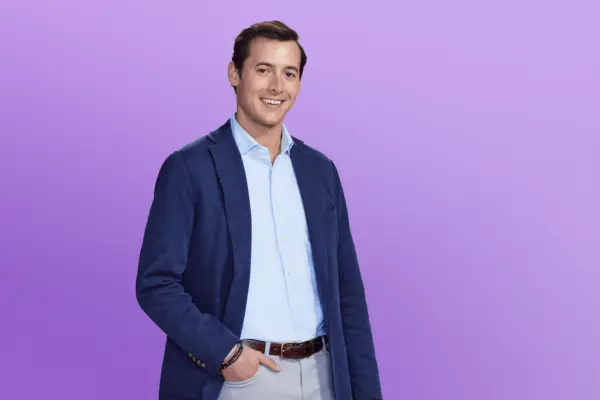 Drake in a dark blue suit posing in front of a purple background