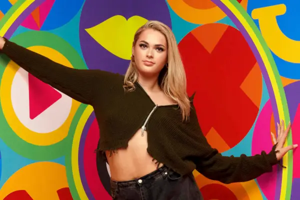 Hallie in Big Brother wearing a brown top, standing in front of a colourful background