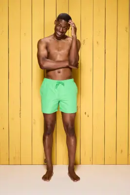 Ayo Odukoya poses in swim shorts in front of a yellow wooden wall for Love Island 2024.
