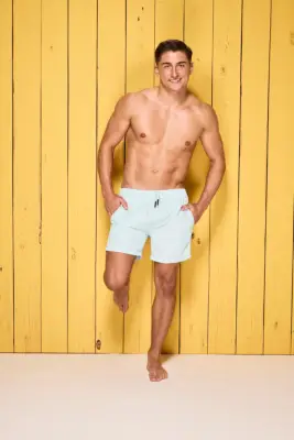 Sean Stone poses in swim shorts in front of a yellow wooden wall for Love Island 2024.