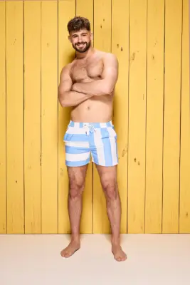 Ciaran Davies poses in swim shorts in front of a yellow wooden wall for Love Island 2024.