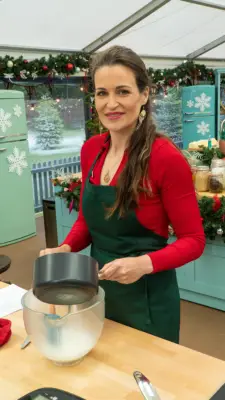 Sophie wearing a red long-sleeved shirt and green apron whilst holding a pot