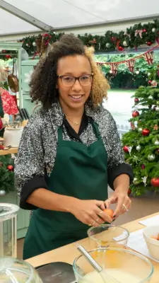 Amelia from Bake Off smiling at the camera wearing a black patterned shirt.