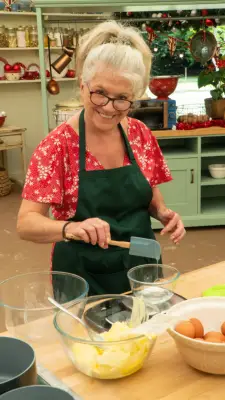 Linda from Bake Off smiling at the camera wearing a red floral shirt.