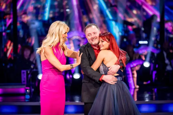 Dianne Buswell and Chris McCausland hugging as they stand in front of Tess Daly.