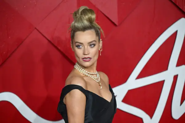 Laura Whitmore wearing a a black gown. She is stood in front of a red background and looking at the cameras