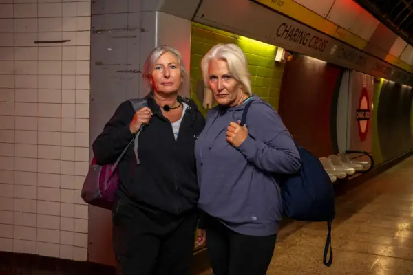 Annida and Cathy stood in exercise clothing in a dimly lit Charing Cross station. They are stood next to each other while looking ahead