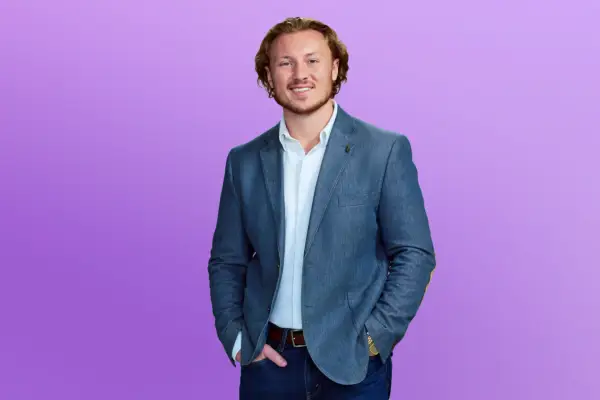 Love Is Blind season 6 star Johnny wearing a suit posing in front of a purple background.