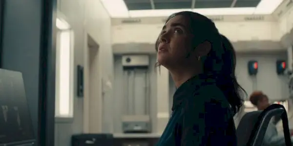 Geraldine Viswanathan as Mel, nervously looking up at the ceiling at her computer desk.