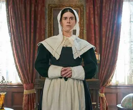 Mary Holland as Patience, a Puritan ghost, standing in a fancy room in CBS sitcom Ghosts