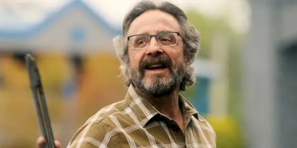 Marc Maron as Mitts standing outside and looking happy while wearing glasses in Stick