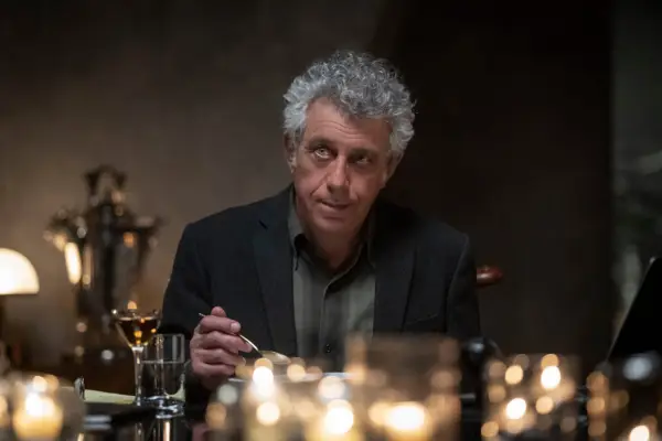 Eric Bogosian as Daniel Molloy in Interview With The Vampire sitting at a candletlit table with a utensil in his hand.