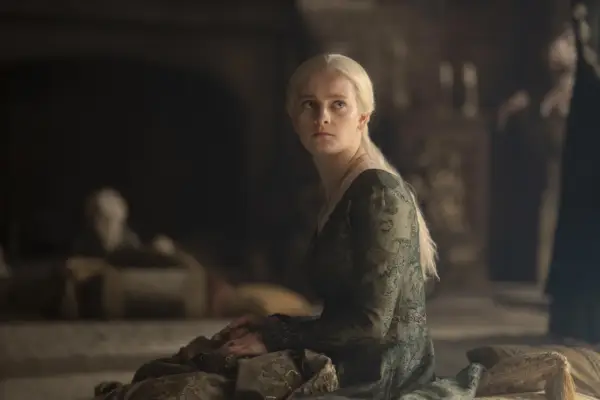 Phia Saban sits and turns on a bed in a green dress as Queen Helaena Targaryen in House of the Dragon season 2.