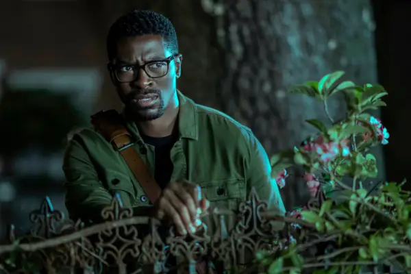 Tongayi Chirisa in Mayfair Witches wearing a green shirt, leaning on a gate