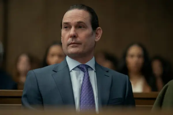 Henry Thomas as Frederick Usher in The Fall of the House of Usher sat in a courtroom wearing a navy suit