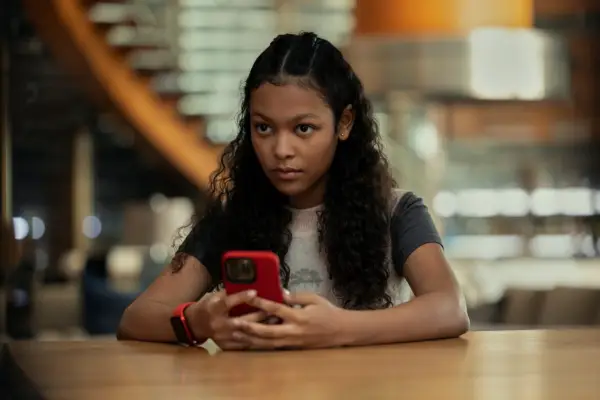 Kyliegh Curran as Lenore Usher in The Fall of the House of Usher sitting at a table, on her phone