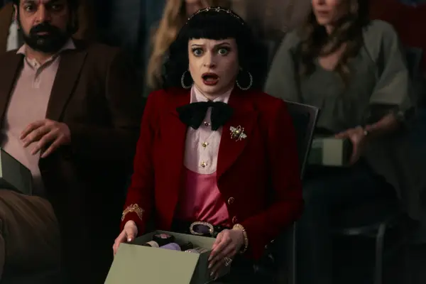 Ruth Codd as Juno Usher in The Fall of the House of Usher sitting down in a red suit, looking shocked