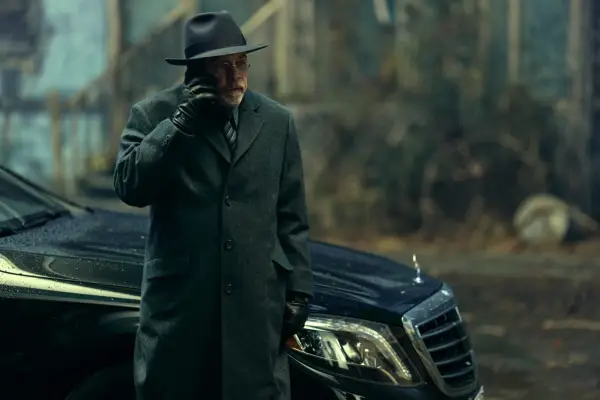 Mark Hamill as Arthur Pym in The Fall of the House of Usher standing by a car in a long dark coat and trilby, with a phone to his ear