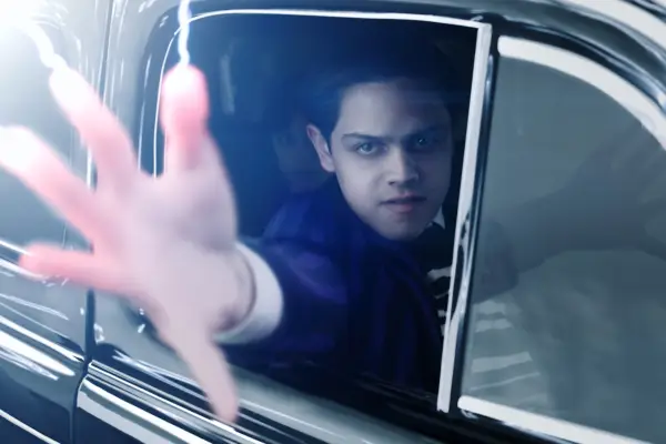 Isaac Ordonez as Pugsley Addams in Wednesday season 2 sitting in a car and holding his arm outside of it, emitting some kind of power.