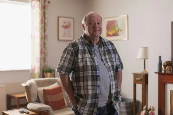 Alex Norton in Two Doors Down, wearing a grey t-shirt and chequered shirt
