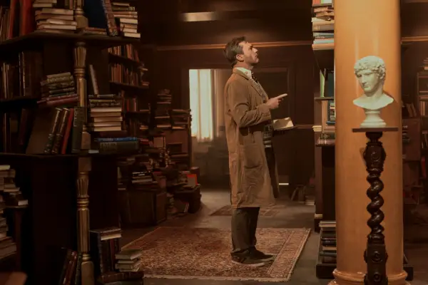 Jon Hamm in Good Omens season 2, looking at a bookshelf
