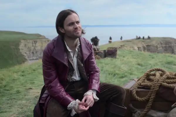 Joey Batey in The Witcher, with long hair and a purple jacket